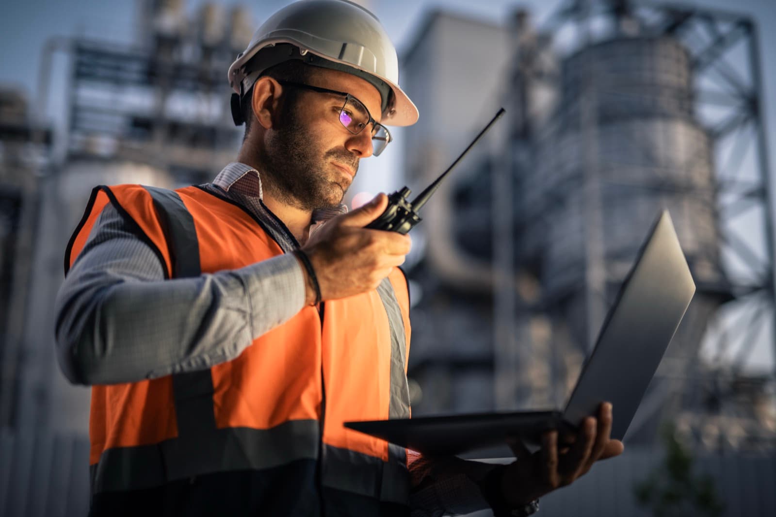 Construction worker using a radio while reviewing information on a laptop